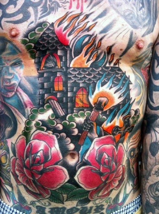 Colorful chest tattoo of a burning church with flames and glowing windows. Surrounded by roses, greenery, and a figure holding a torch.