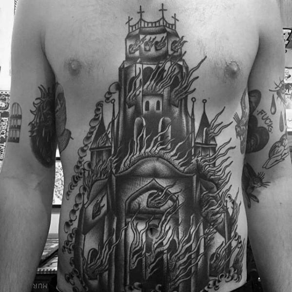 Large black and grey tattoo of a burning cathedral covering the chest and stomach. Intricate flames and gothic details create a powerful design.