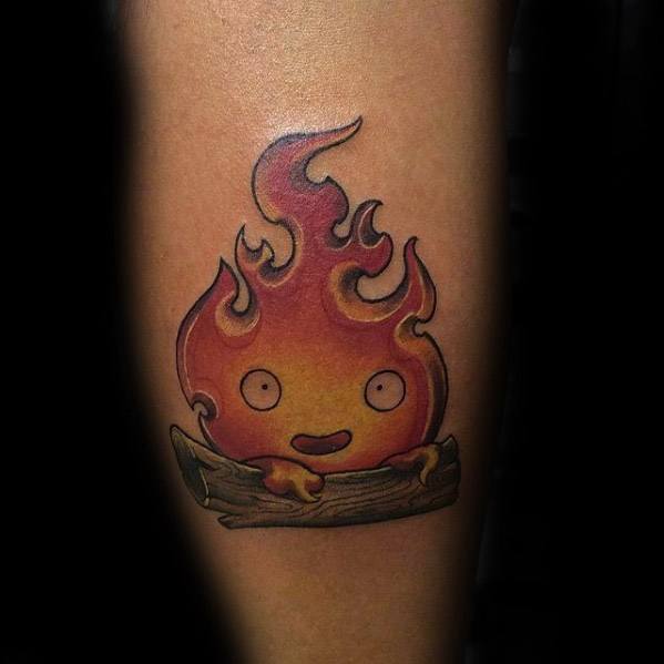 Playful Calcifer tattoo with swirling flame tips, a happy face, and small hands resting on a wooden log base.