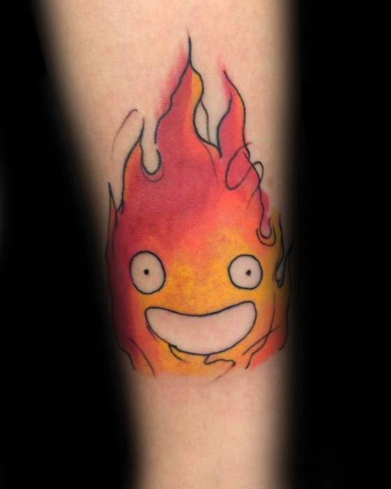 Vibrant Calcifer tattoo with soft red and orange blending, bold eyes, wide smile, and thin flame outlines for a dreamy look.