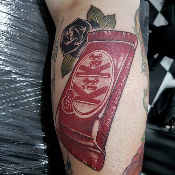 Realistic Kit Kat tattoo with detailed shading and highlights, featuring a partially unwrapped bar alongside black roses for a bold contrast.