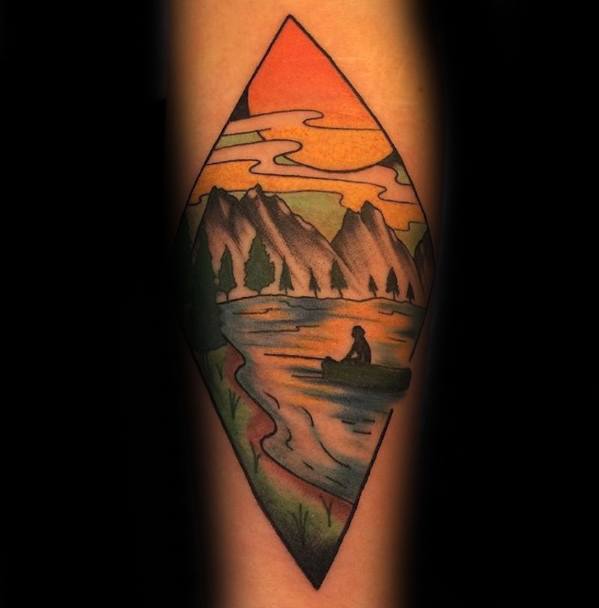 Alt text: Tattoo in a diamond shape showing a serene lake scene with mountains, a canoe, and a sunset, all done in warm, vibrant colors.