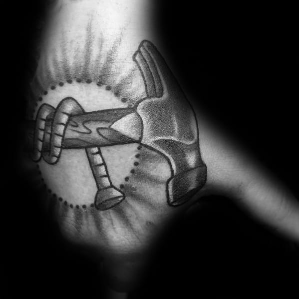 Black and gray tattoo of a hammer and nail with a radiating design, symbolizing strength, craftsmanship, and dedication to woodworking.