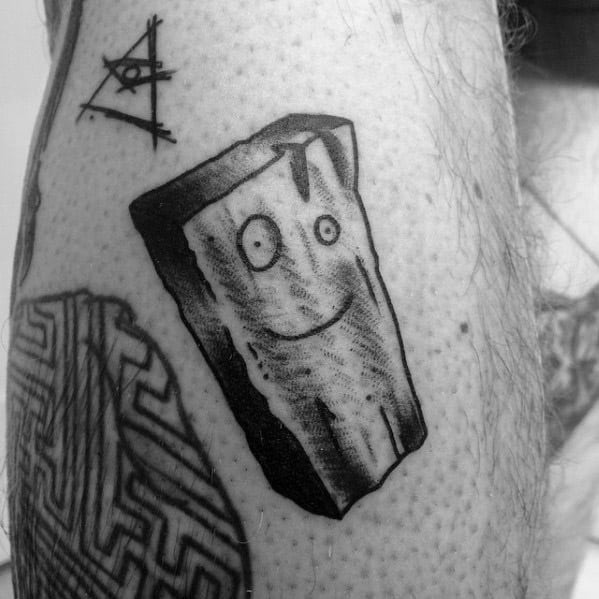 Black and white tattoo of Plank from Ed, Edd n Eddy with a sketchy, textured style and simple smiling face on a piece of wood.