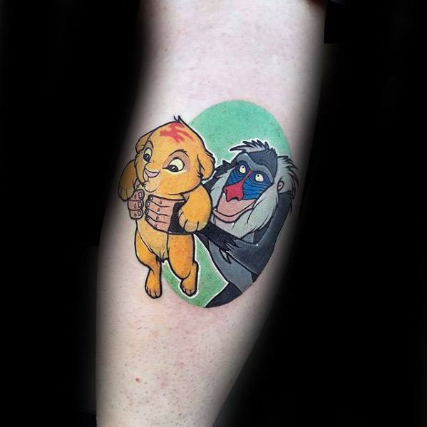 Colorful tattoo of Rafiki holding up baby Simba from The Lion King, with a bright green background in an oval frame on the leg.