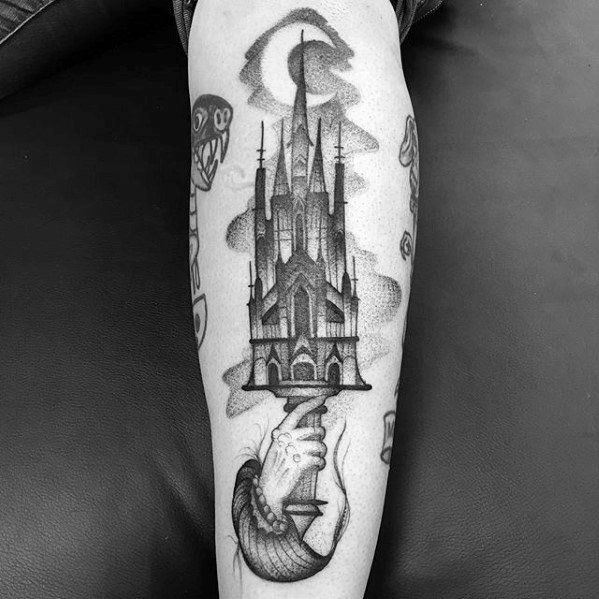 Surreal blackwork tattoo of a gothic cathedral held by a hand emerging from a serpent’s body, with clouds and crescent moon above.