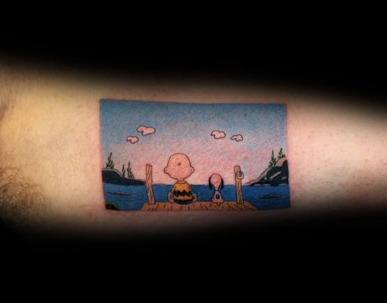 Small, colorful Charlie Brown and Snoopy tattoo featuring them sitting on a dock, gazing at a peaceful lake, symbolizing friendship and tranquility.