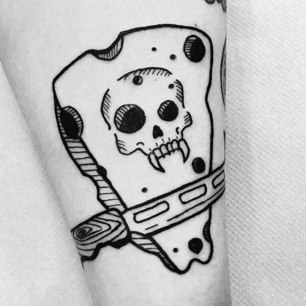 Black and white tattoo of a cheese wedge with a skull face carved into it, pierced by a wooden stake, featuring bold outlines and fine details.