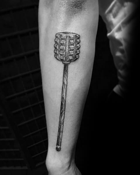 Black and gray tattoo of a chocolate mallet with detailed shading, giving it a realistic and bold appearance on the forearm.
