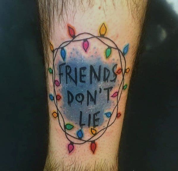 Christmas tattoo inspired by *Stranger Things*, featuring the phrase "Friends Don't Lie" surrounded by colorful holiday lights, blending festive and pop culture elements.