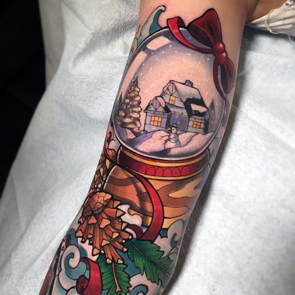 Christmas tattoo of a festive snow globe featuring a cozy winter cabin, snowman, and decorated tree, adorned with ribbons, pinecones, and holly.