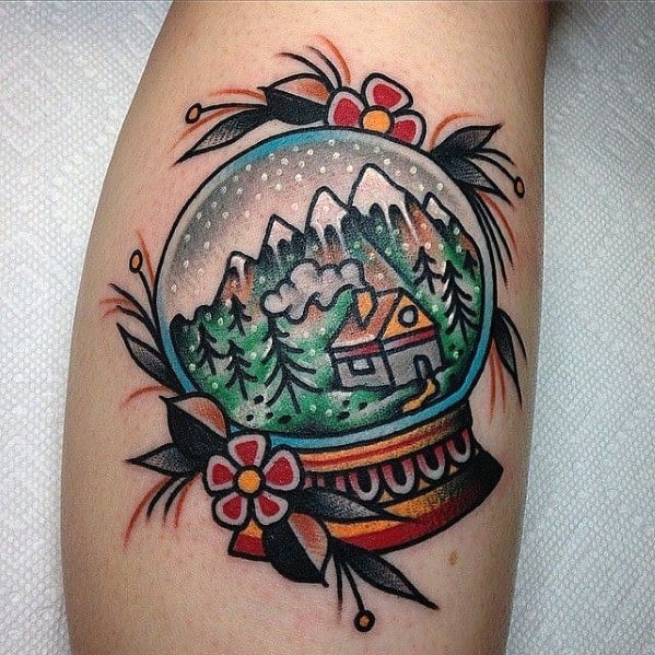 Traditional-style Christmas tattoo of a snow globe featuring a cozy cabin in a snowy mountain landscape, surrounded by floral and decorative elements.