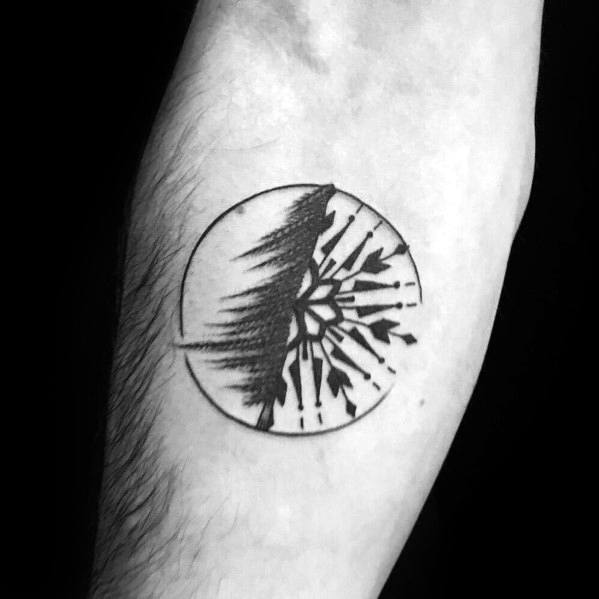 Abstract Christmas tree tattoo with a circular design, featuring a split effect of a forest and geometric snowflake pattern on the forearm.