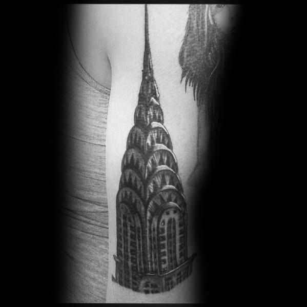 Black-and-grey Chrysler Building tattoo with bold shading and fine details, creating a striking architectural design on the upper arm.