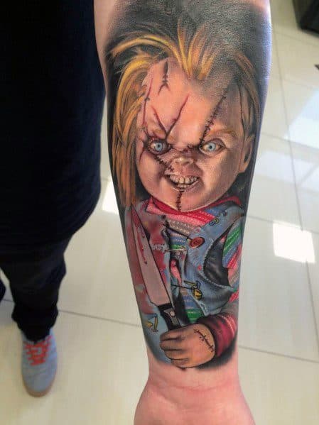 Realistic Chucky tattoo with vivid colors, showing his sinister grin, stitched face, and a bloodied knife for a striking horror-themed design.