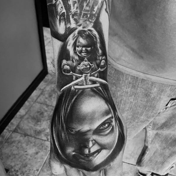 Black and grey Chucky tattoo with eerie shading, featuring his sinister grin, a jack-in-the-box clown, and a hauntingly detailed horror design.