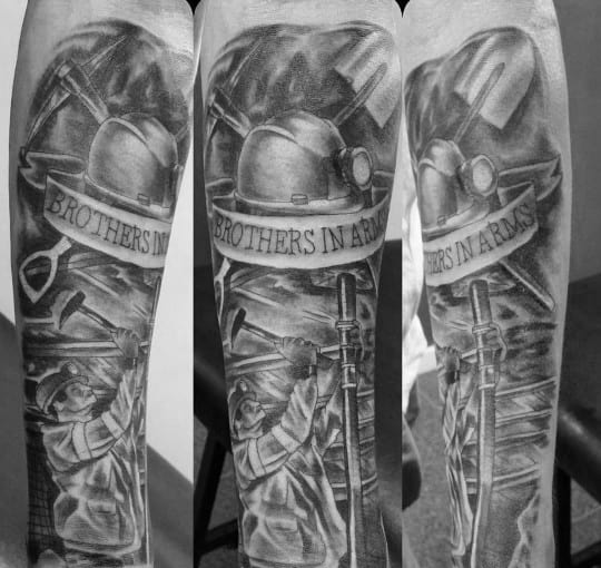 Black and grey forearm tattoo of coal miners at work with helmets, tools, and a banner reading "Brothers in Arms."