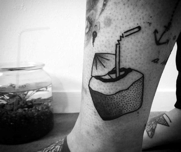 Minimal blackwork tattoo of a cut coconut drink with straw and umbrella, featuring bold shading and clean lines on the lower leg.