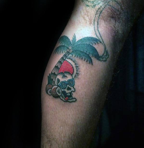 Small colorful tattoo of a coconut wearing sunglasses under a palm tree with a red sun in the background, inked on the leg.
