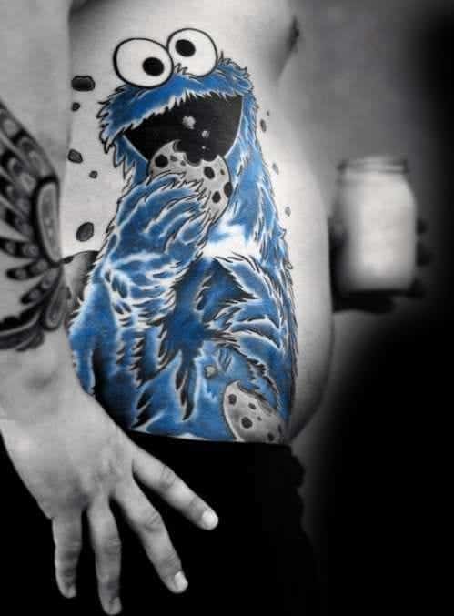 Large Cookie Monster side tattoo in vivid blue, happily devouring cookies with crumbs flying across a black and white background.