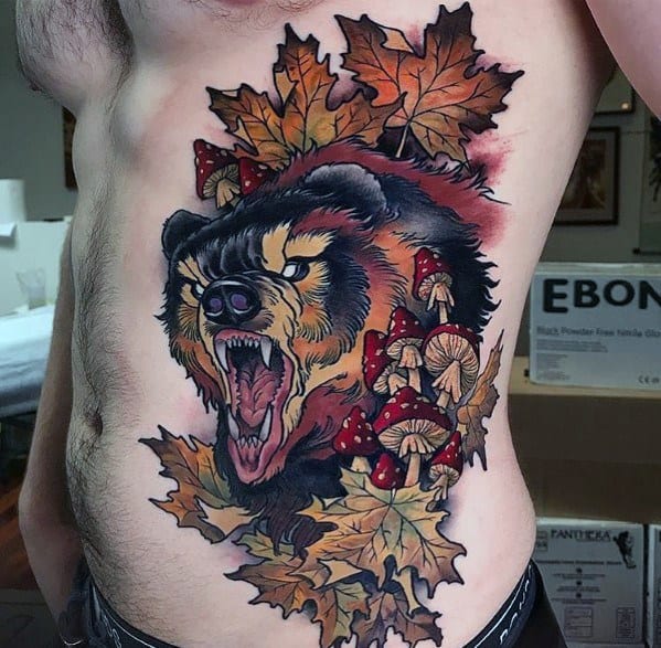 Vibrant ribcage tattoo featuring a snarling bear surrounded by autumn leaves and detailed mushrooms, with bold shading and rich colors.