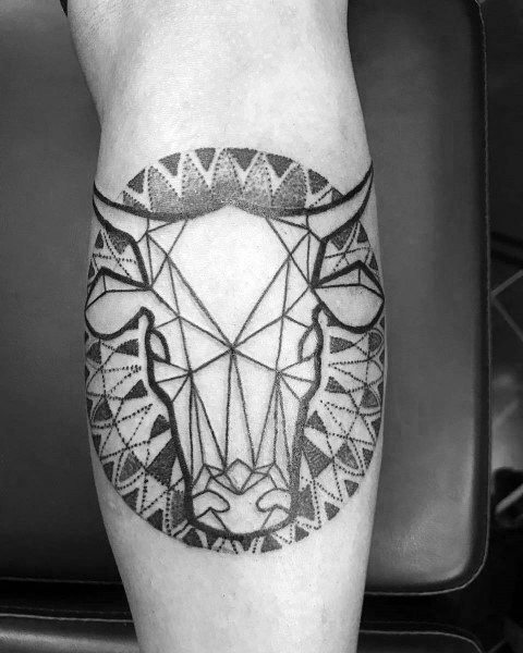 Geometric cow head tattoo with bold linework and tribal-inspired dotwork patterns, forming a symmetrical design on the calf.