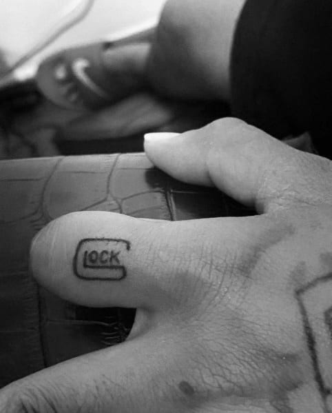 Small black ink tattoo of the Glock logo on the thumb, featuring a simple and bold design for a subtle yet impactful statement.