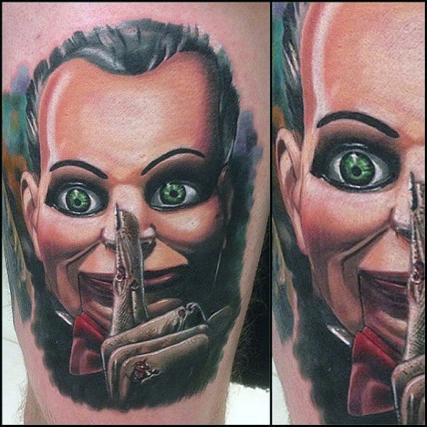 Realistic color tattoo of Billy the puppet from *Dead Silence*, featuring eerie green eyes, lifelike shading, and a chilling "shush" gesture for a haunting effect.