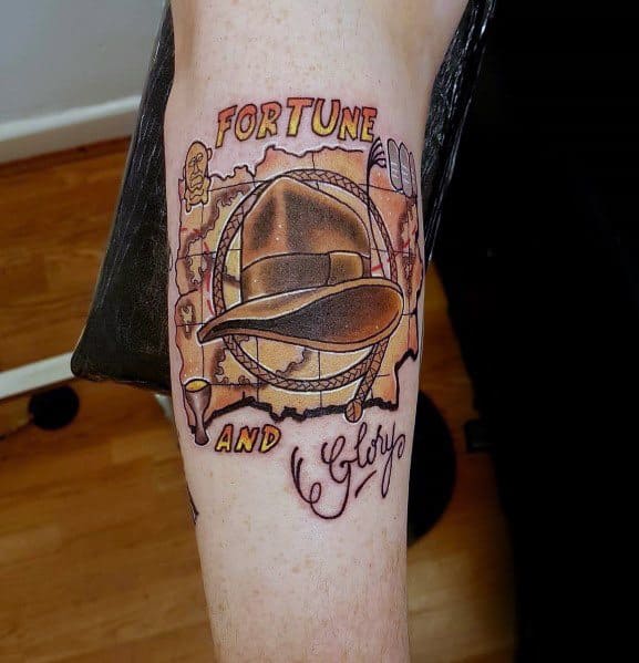 Indiana Jones tattoo featuring his iconic hat, whip, and map, with 'Fortune and Glory' inscribed in bold lettering.