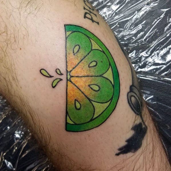 Vibrant lime wedge tattoo with bold green and yellow shading, featuring juice droplets for a fresh and dynamic citrus-inspired design.