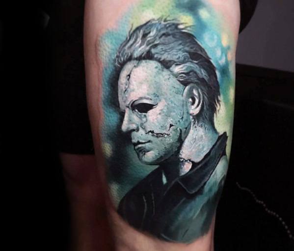 Vibrant Michael Myers tattoo with a cracked mask, featuring eerie green and blue tones for a haunting, cinematic horror effect.