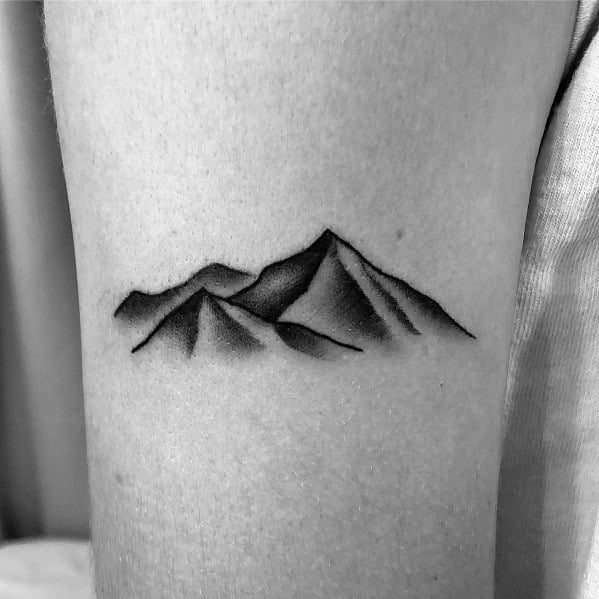 Minimalist mountain tattoo on the arm, featuring shaded peaks with a soft gradient effect for a subtle and natural look.
