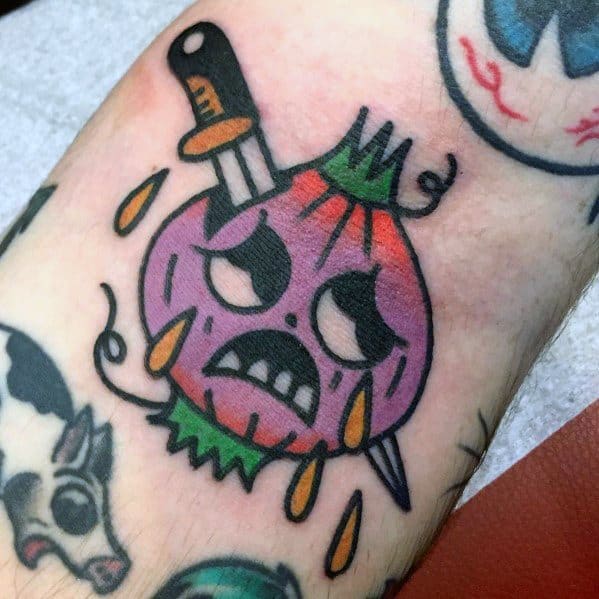 Bold neo-traditional onion tattoo featuring a crying, angry-faced onion with a dagger stabbed through it, dripping tears and vibrant colors.