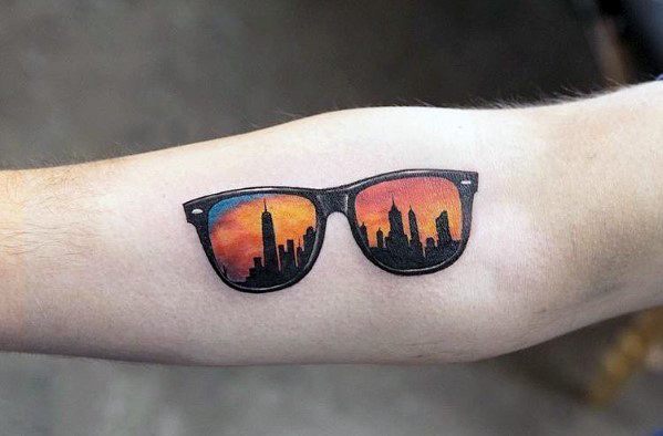 Tattoo of sunglasses reflecting a city skyline at sunset, blending urban aesthetics with vibrant colors for a stylish and modern design.
