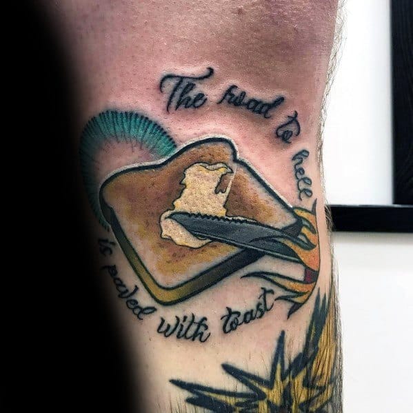 Creative toast tattoo with a flaming butter knife and the phrase "The road to hell is paved with toast," blending humor with bold artistry.