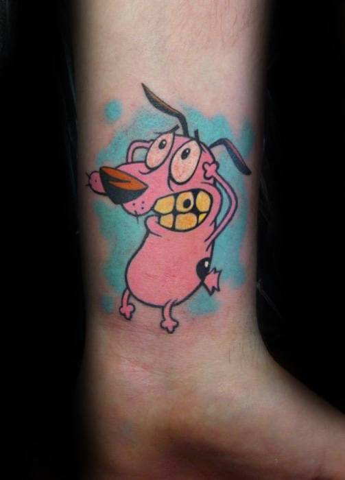 Tattoo of Courage the Cowardly Dog in a panicked pose with clenched teeth, set against a soft blue splash background near the ankle.