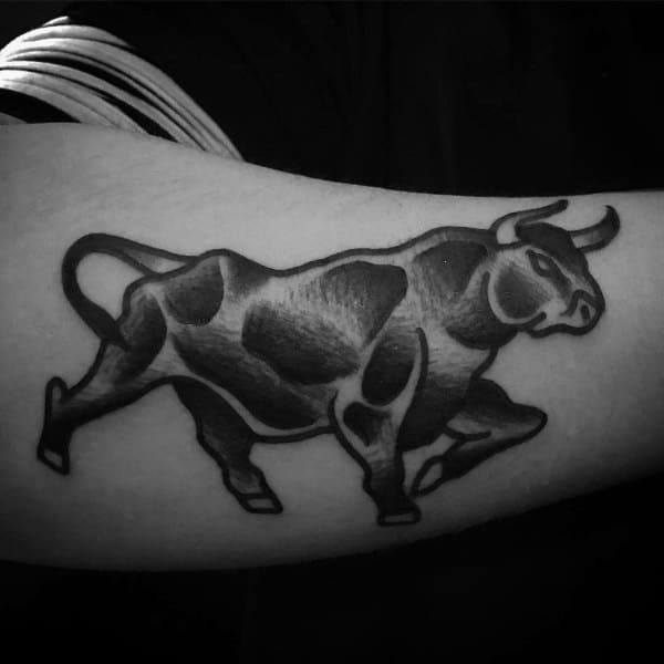 Bold black and grey bull tattoo in a dynamic pose, featuring strong shading and a muscular, stylized form on the forearm.