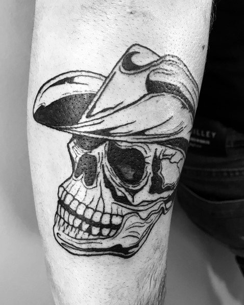 Black ink tattoo of a cowboy skull wearing a tilted hat, done in a bold, illustrative style with strong linework and shading for a rugged look.