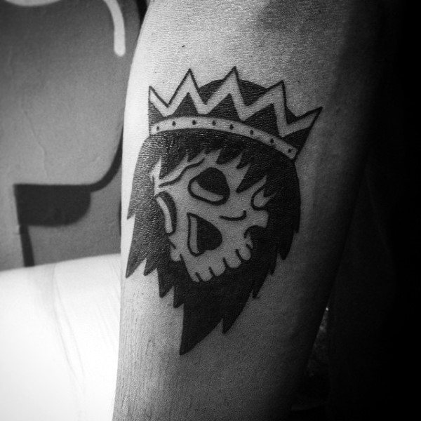 Tattoo of a crowned skull with flowing hair on the inner arm, black and grey shaded