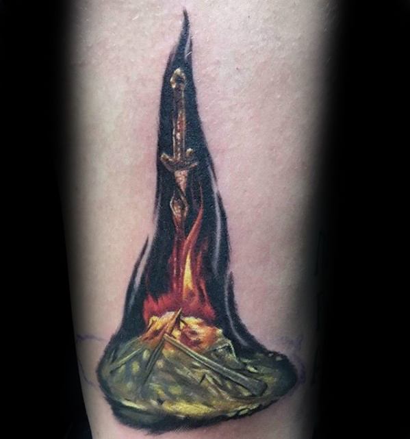 Realistic Dark Souls bonfire tattoo with a sword embedded in burning embers, surrounded by ash and a dark flame aura.
