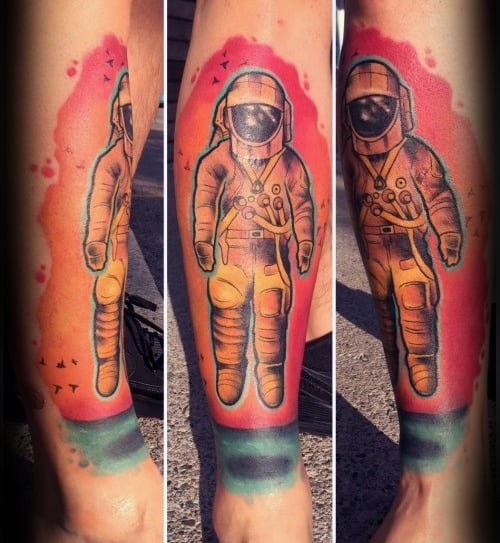 Colorful Deja Entendu astronaut tattoo wrapping around the leg, with a pink-orange sky, teal ocean, and black bird silhouettes.