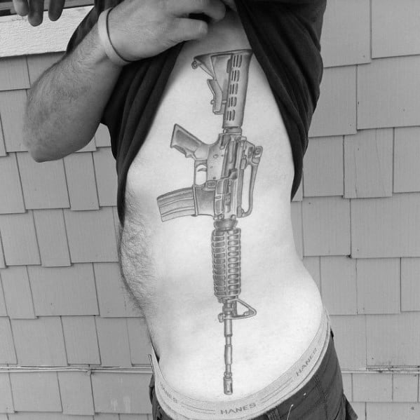 Large black and grey AR-15 tattoo on the ribcage, featuring intricate details and realistic shading, symbolizing strength, precision, and tactical readiness.