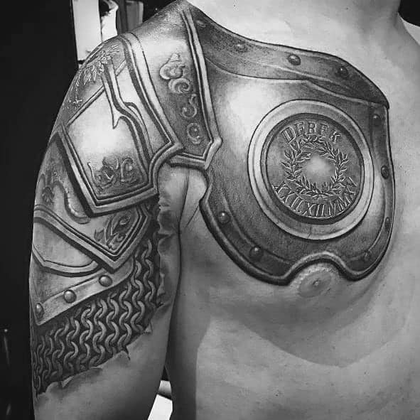 Black and grey shoulder and chest tattoo featuring realistic Roman-style armor with intricate engravings, chainmail details, and a bold, metallic finish.