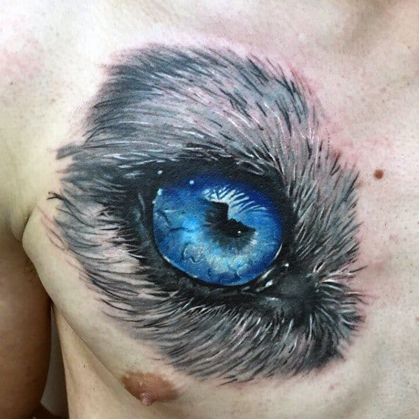 Hyper-realistic Siberian Husky eye tattoo on a man's chest, featuring intense blue hues and intricate fur details for a striking 3D effect.