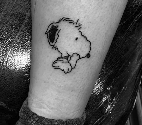Black and white tattoo of Snoopy in a thoughtful pose, resting his chin on his paw, placed on a person's arm.