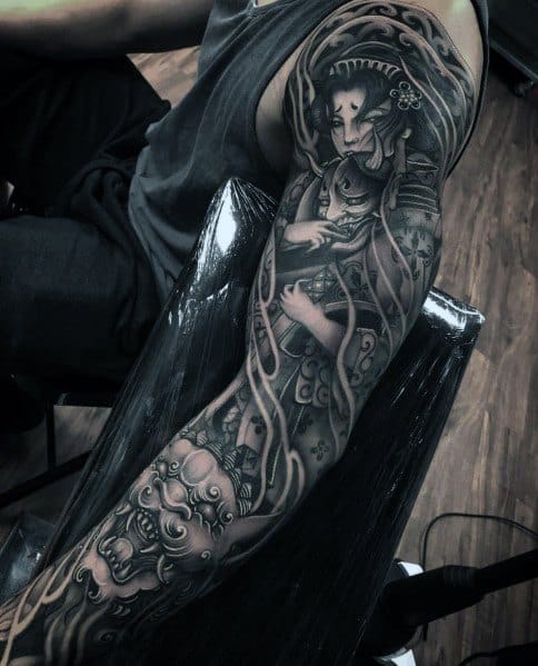 Full-sleeve tattoo in black and grey featuring a detailed geisha holding a mask, flowing patterns, and a fierce guardian lion for a traditional Japanese theme.