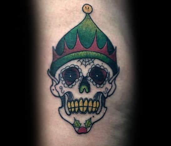 Christmas tattoo of a skull wearing a festive elf hat, blending holiday cheer with a spooky twist, featuring holly details and sugar skull-style accents.