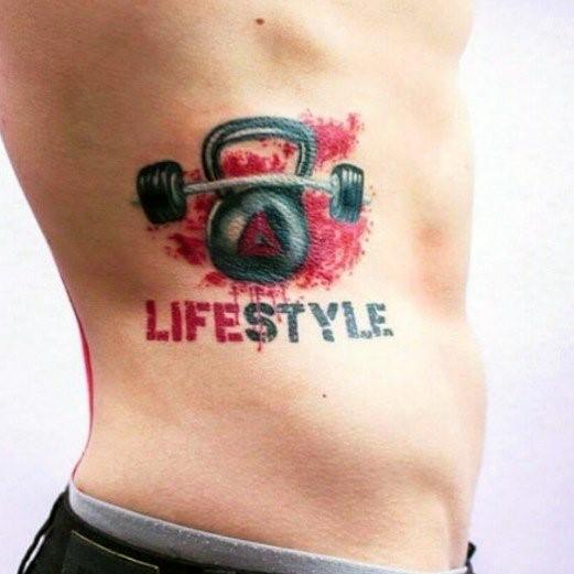 Vibrant CrossFit tattoo on the ribs featuring a kettlebell-barbell fusion with red splashes and bold "LIFESTYLE" text, symbolizing strength and dedication.