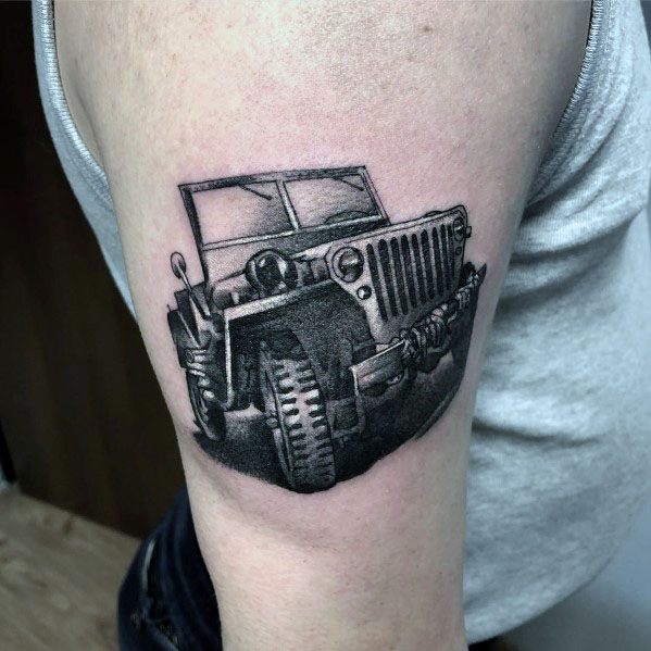 Black and grey Jeep tattoo on the upper arm, featuring a detailed off-road Jeep with rugged tires and shading for a realistic, bold design.