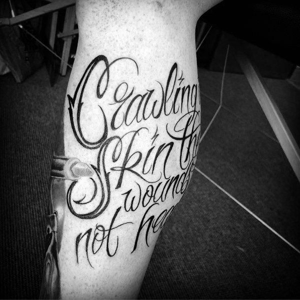 Black ink tattoo featuring lyrics from Linkin Park's 'Crawling' in an elegant script font, wrapping around the leg.